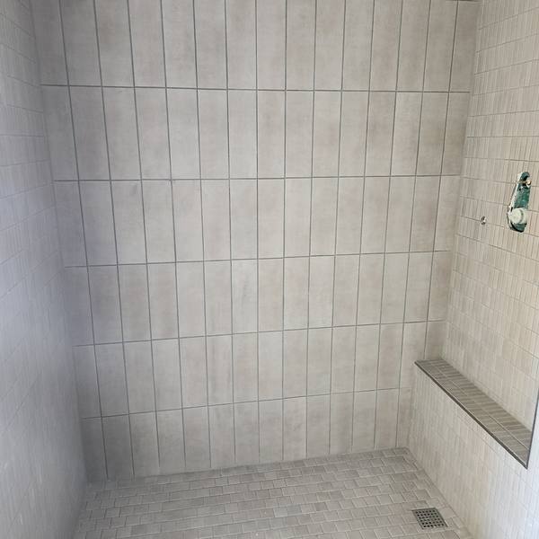 Shower with gray vertical wall tile, mosaic floor, and bench