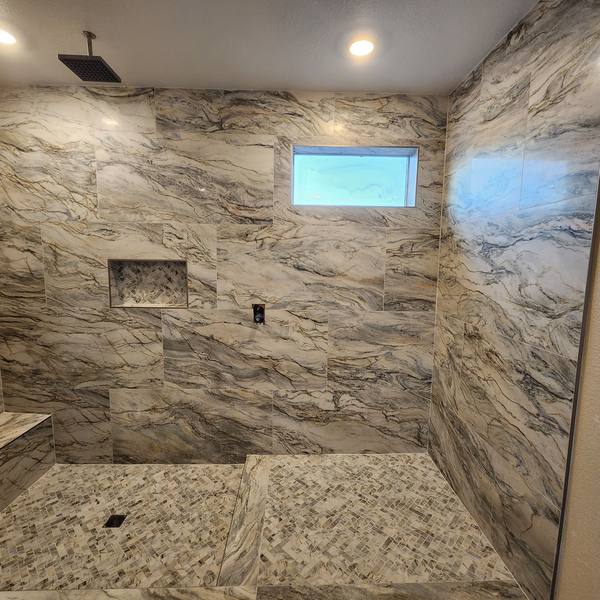 Walk-in shower with marble-look tile, niche, and bench