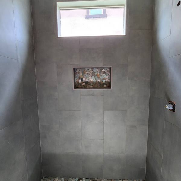 Shower with gray wall tile, pebble floor, and window