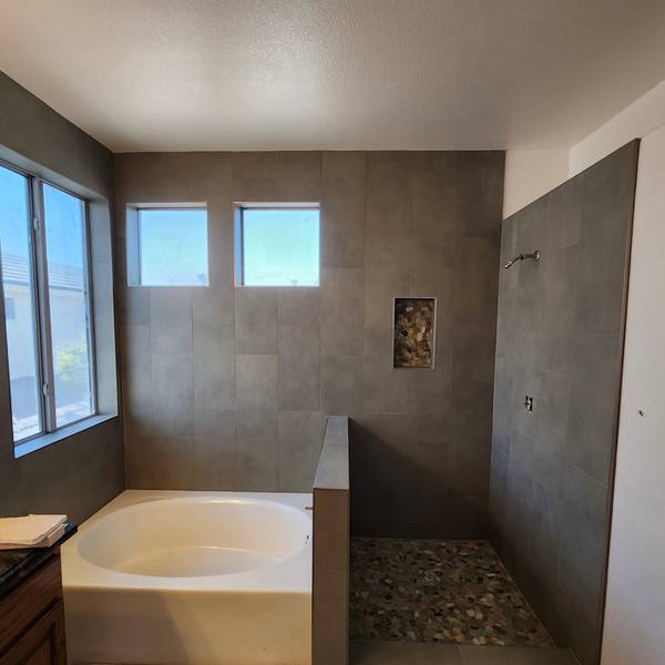 Walk-in shower with a pebble floor next to a tub