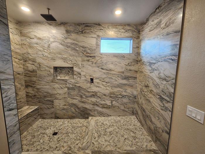 Walk-in shower with marble-look wall tile, niche, and bench